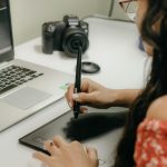 A woman using a digital tablet and stylus next to a laptop, showcasing modern design technology.