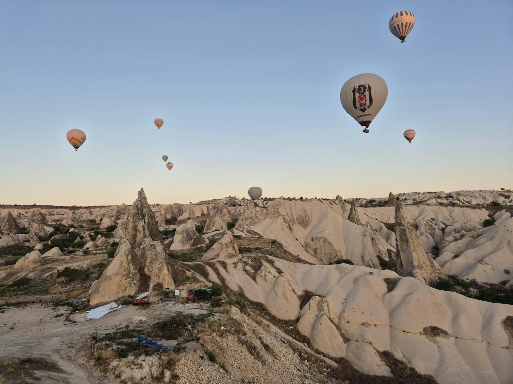Aerial view of hot air balloons floating above the rocky formations of Cappadocia at sunrise.