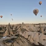 Aerial view of hot air balloons floating above the rocky formations of Cappadocia at sunrise.