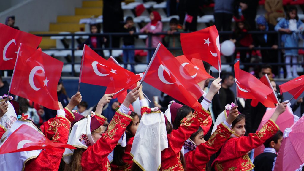 Children dressed in traditional attire waving Turkish flags during a national celebration in İstanbul.