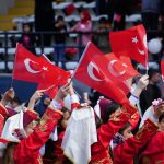 Children dressed in traditional attire waving Turkish flags during a national celebration in İstanbul.