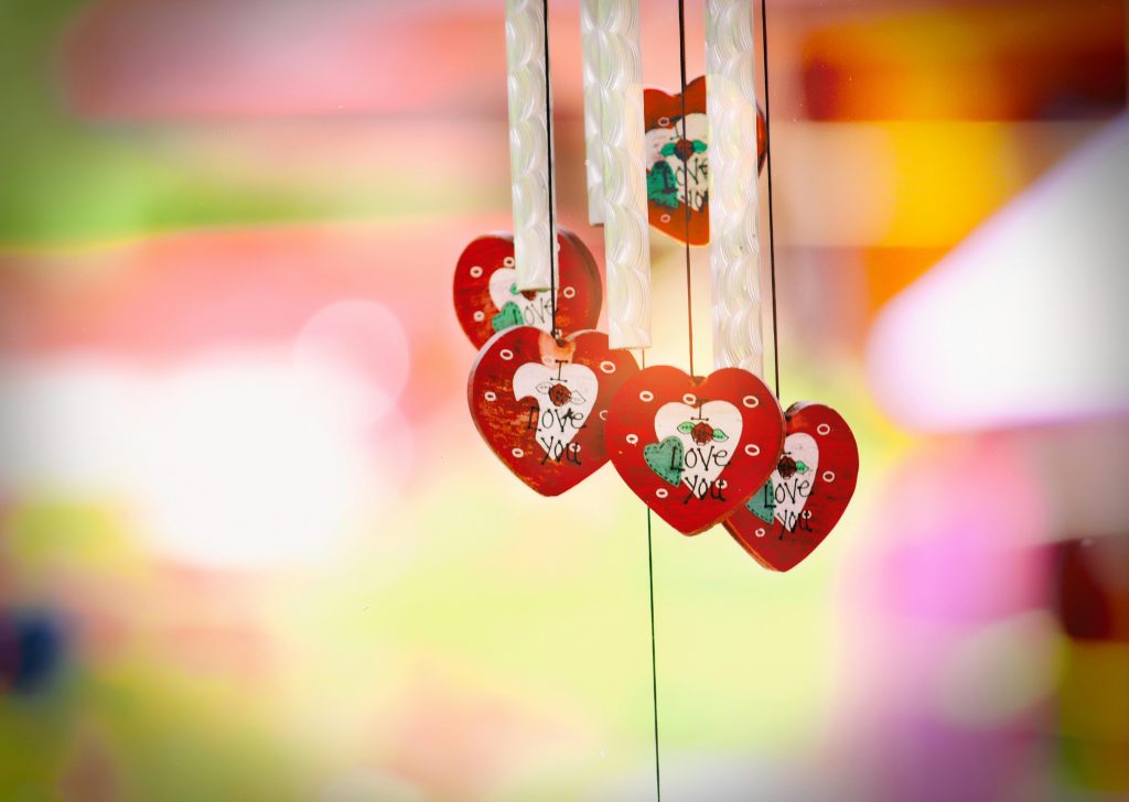 Vibrant heart-shaped decorations with love message hanging against a colorful blurred background.