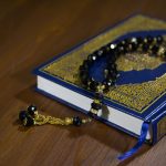 Islamic holy book, Quran, with black prayer beads on a wooden table, symbolizing faith and spirituality.