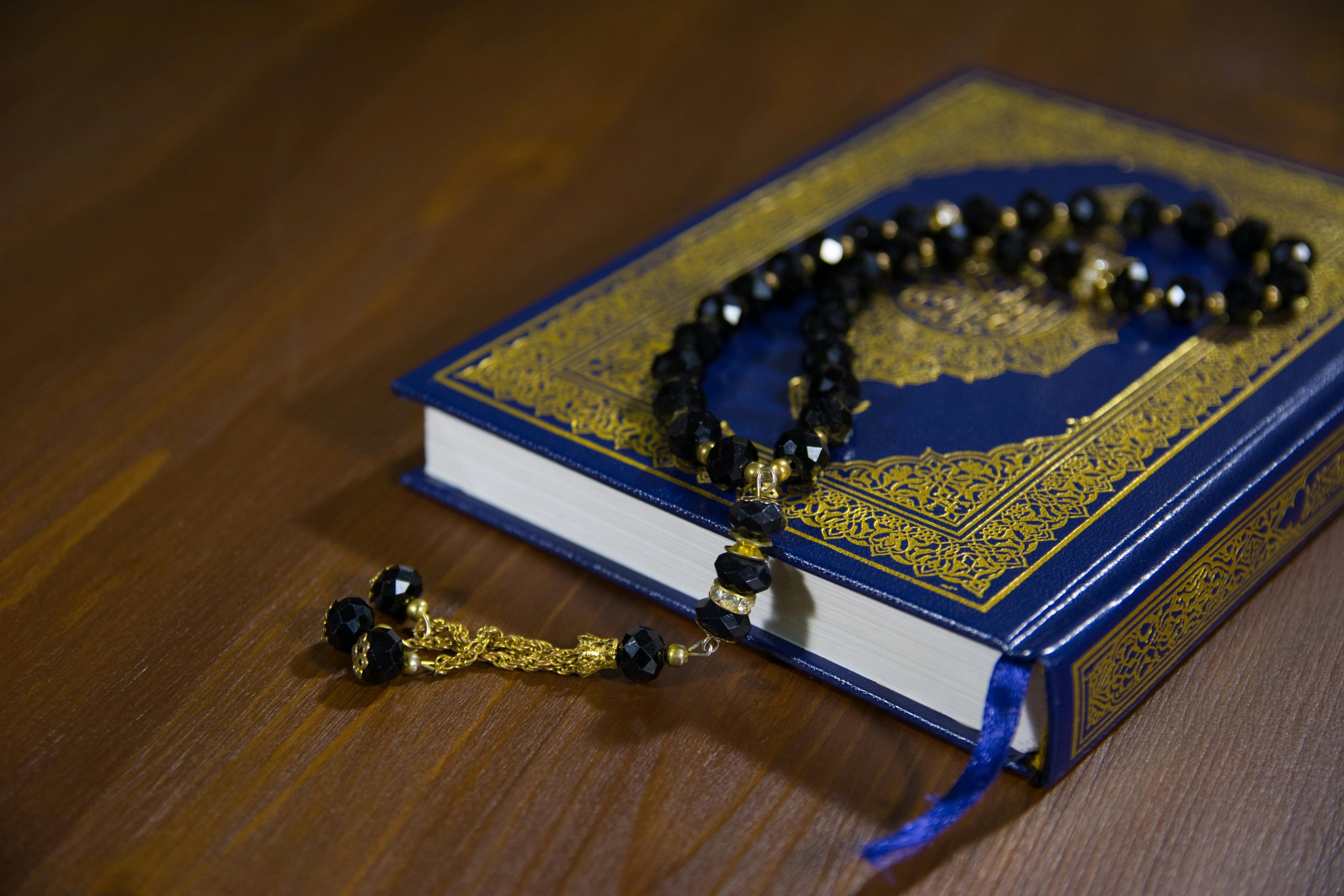 Islamic holy book, Quran, with black prayer beads on a wooden table, symbolizing faith and spirituality.