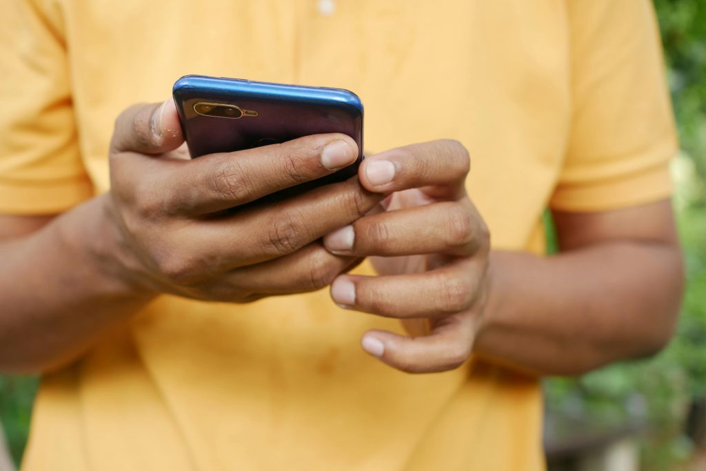 Close-up of a person in an orange shirt using a smartphone outdoors.
