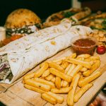 Close-up of a hearty Turkish wrap served with crispy fries and dipping sauce.