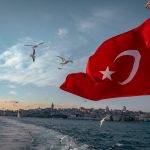 Turkish flag flutters above Istanbul's skyline with seagulls flying over the Bosphorus.