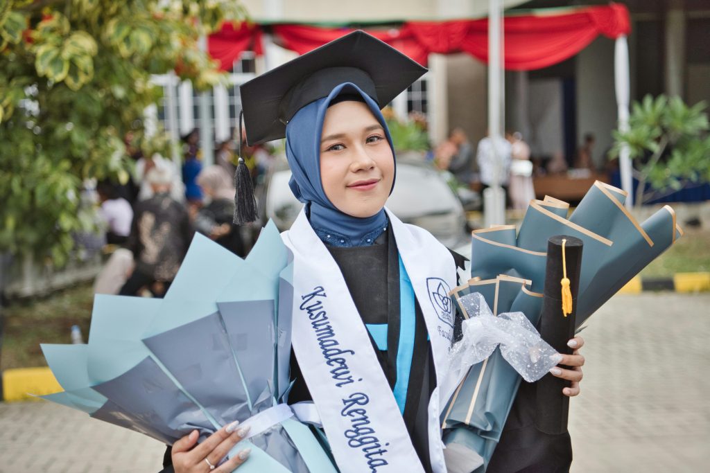 Smiling young graduate holding diplomas and wearing a hijab outdoors.