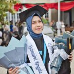 Smiling young graduate holding diplomas and wearing a hijab outdoors.