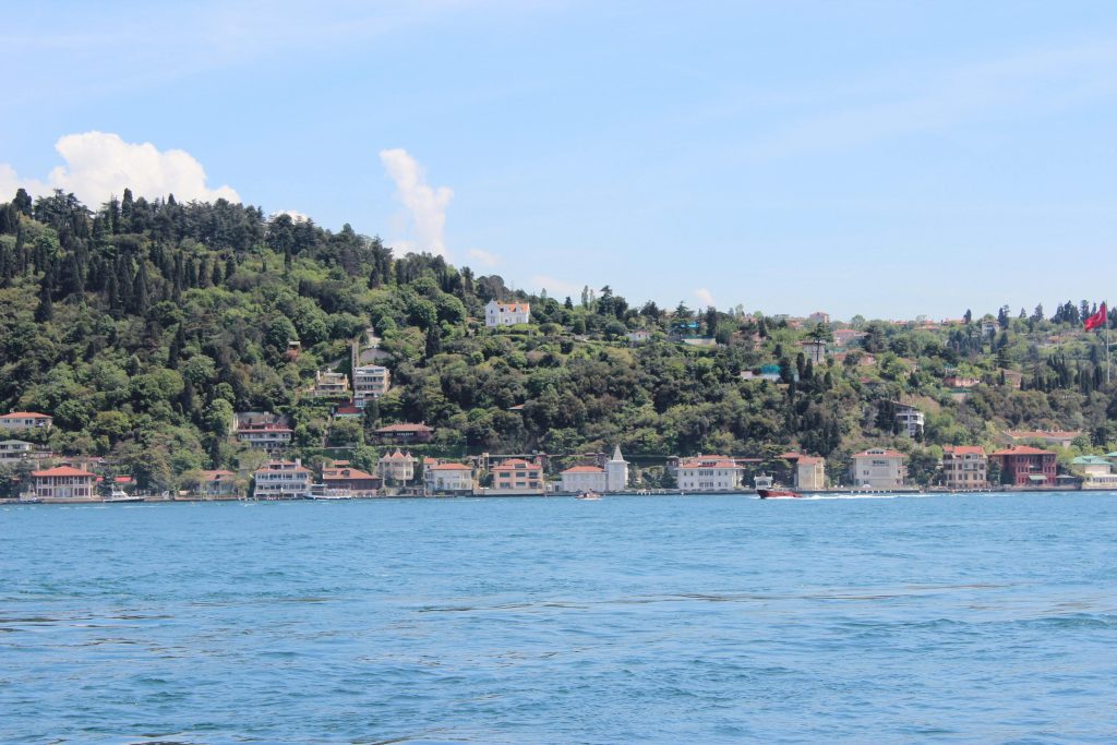 Scenic view of İstanbul's Bosphorus waterfront with lush green hills and blue waters.