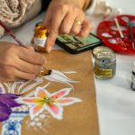 Artist painting vibrant flowers on paper using gouache paints in an indoor setting.