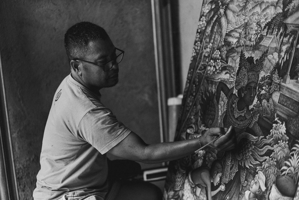 An artist skillfully paints a detailed Balinese canvas in monochrome.