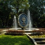 Fountain with the Institut Pertanian Bogor emblem surrounded by vibrant greenery and trees.