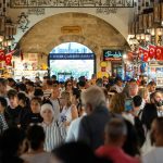 A crowded scene inside the vibrant Istanbul Spice Bazaar with people shopping and Turkish flags hanging.
