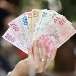 A hand displays several denominations of Turkish Lira banknotes in an outdoor setting, showcasing currency diversity.