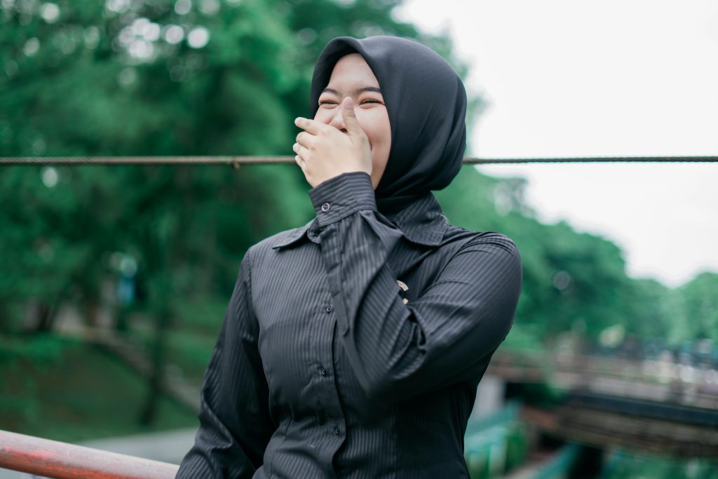 A happy Muslim woman in a black hijab laughs joyfully outdoors in Banten, Indonesia.