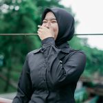 A happy Muslim woman in a black hijab laughs joyfully outdoors in Banten, Indonesia.
