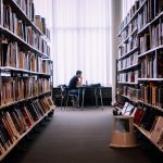 A person studies alone in a peaceful library filled with books, capturing a quiet moment of learning.