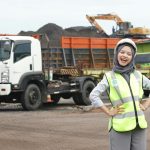 Female worker with safety gear at a bustling construction site with trucks and excavators.