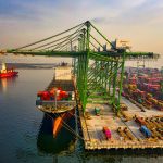 A bustling aerial view of a container port in North Jakarta, Indonesia with ships and cranes.