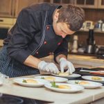 Chef meticulously plating dishes in a kitchen setting, showcasing culinary art.