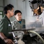 Two technicians in a workshop in Indonesia operating a CNC machine, focused on precision engineering.