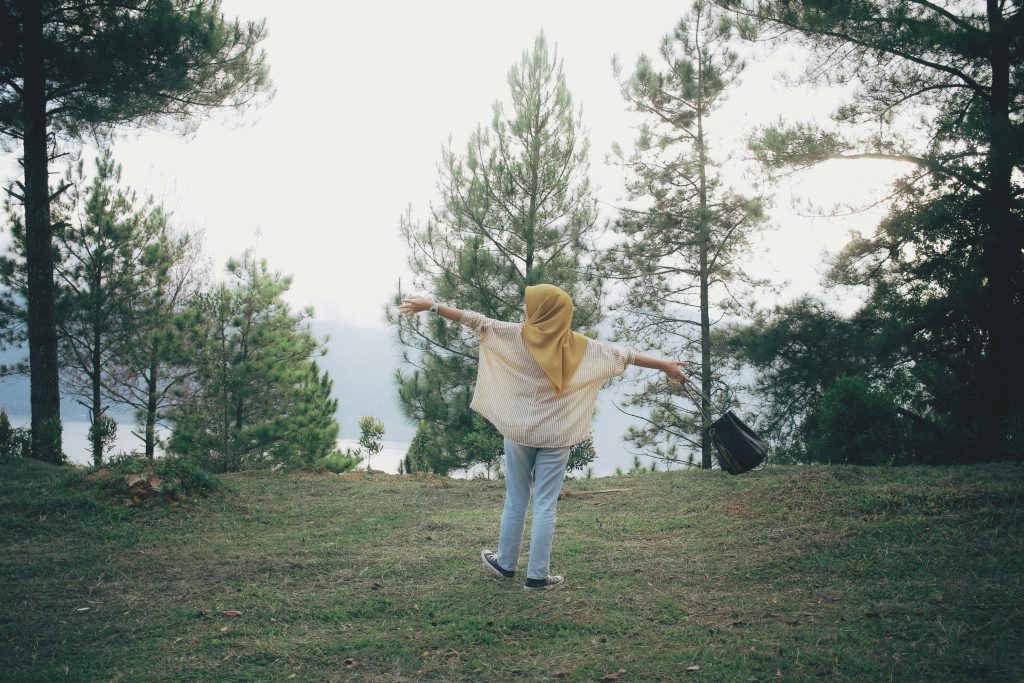 A woman with outstretched arms enjoys nature in a peaceful forest setting, symbolizing freedom and tranquility.