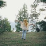 A woman with outstretched arms enjoys nature in a peaceful forest setting, symbolizing freedom and tranquility.