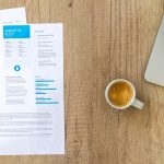 Top view of a desk with resume, coffee cup, and laptop on a wooden surface, ideal for business concepts.