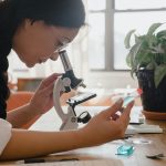 Woman examining sample under microscope in a lab, emphasizing research.