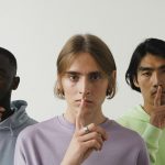 Three young adults making a shushing gesture in a studio setting, highlighting diversity.