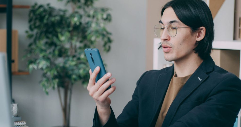 A man in glasses using a smartphone in his office. Modern technology meeting workspace environment.