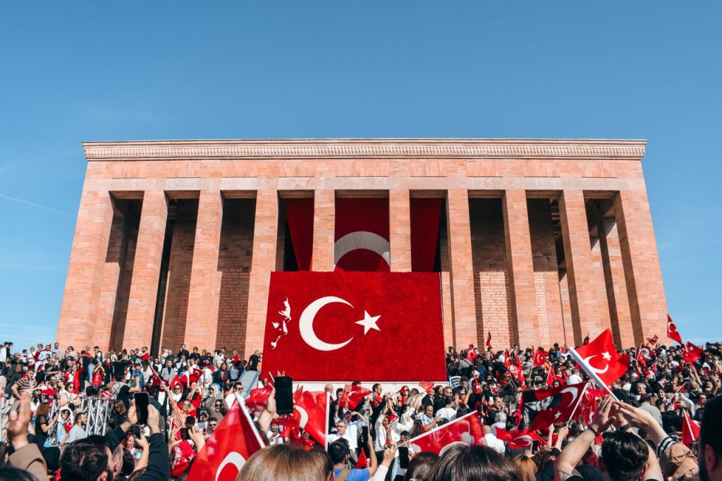 Crowd with Turkish flags at Anıtkabir in Ankara on a clear day, showcasing national pride.